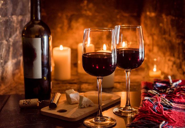 two glasses and a bottle of red with candles
