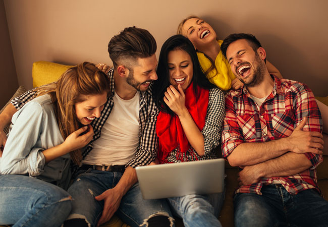 five friends laughing around a computer together
