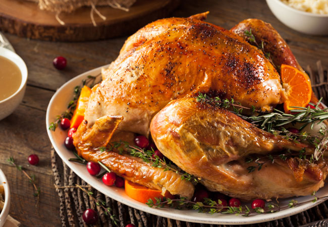 A serving platter with a full, roasted turkey, garnished with rosemary. 