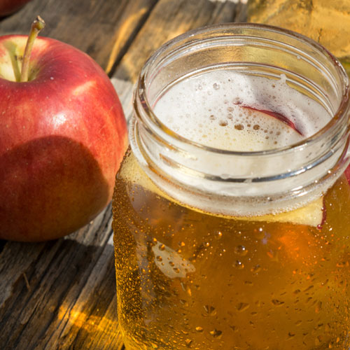 Apple cider in a mason jar next to an apple on a wood table.