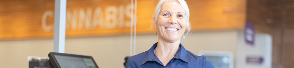 NSLC team member is smiling standing at the checkout ready to help customers.