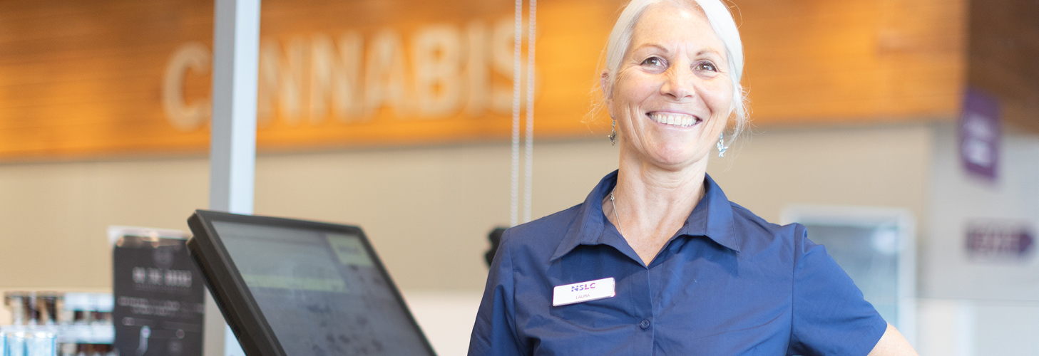 NSLC team member is smiling standing at the checkout ready to help customers.