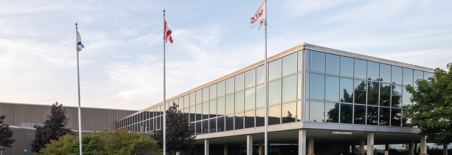Picture of the exterior of the NSLC Head Office Building. The Head Office building has mirrored glass on the outside with three flags at full mast. 