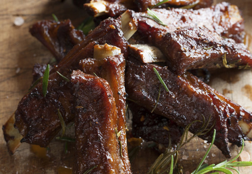 3 barbecue sauce-smothered ribs stacked on a wooden plank 