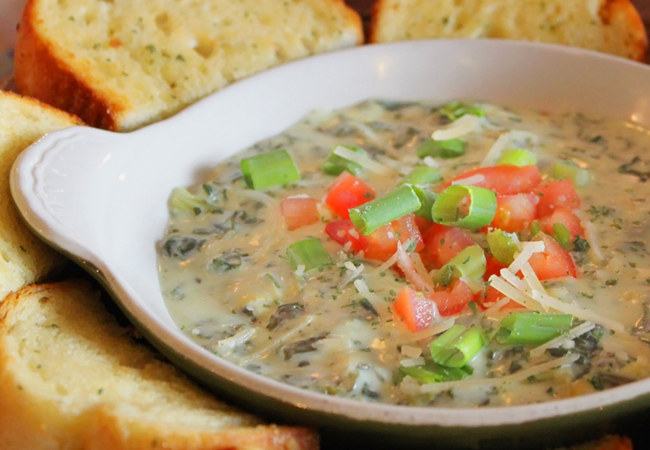 A small bowl of crab artichoke cheese dip surrounded by garlic bread
