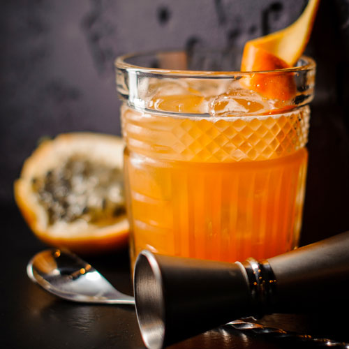 A mixed orange drink in a ornate glass garnished with an orange curl.