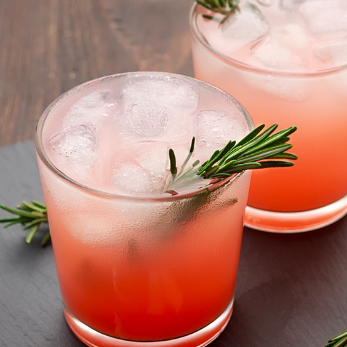 Two red mixed drinks with ice and garnished with rosemary. 