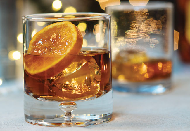 Two glasses with a mixed drink on the rocks with candied orange slice.