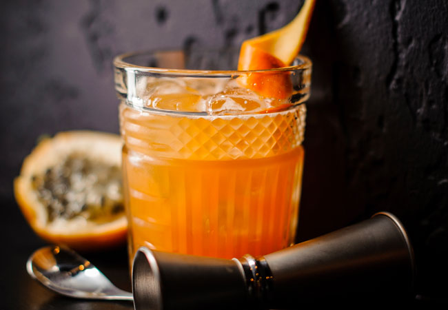 A mixed drink in an ornate glass garnished with an orange twist. 