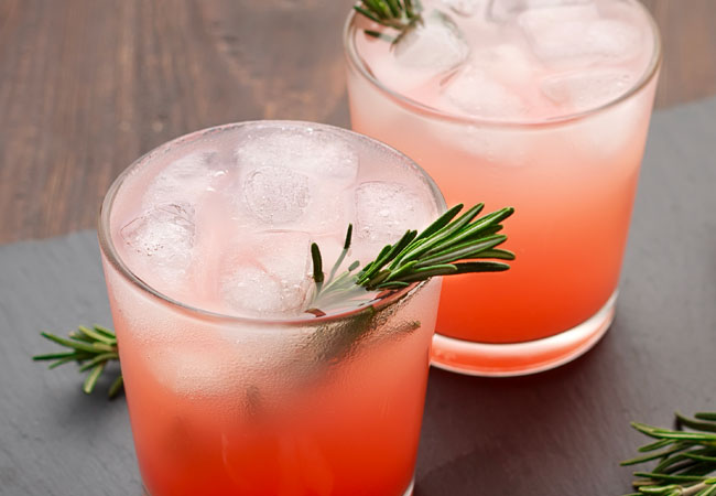 Two red mixed drinks topped with ice and garnished with rosemary.