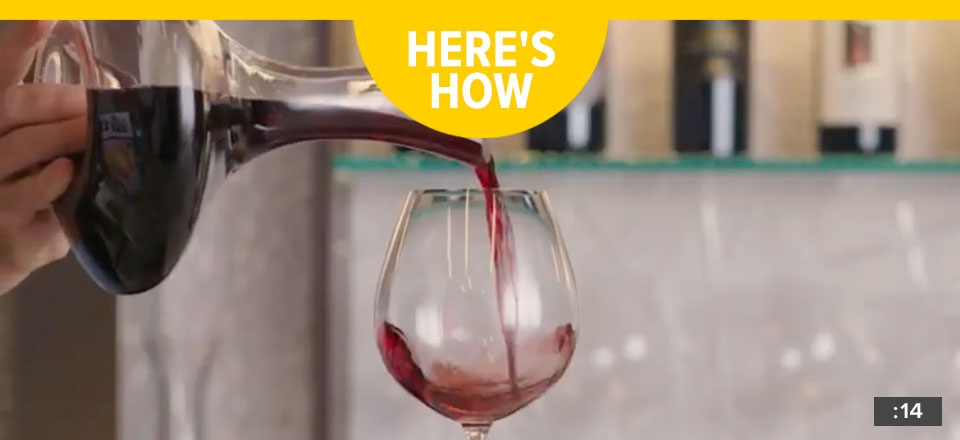 Red wine being poured from a decanter into a wine glass with the words "Here's How".