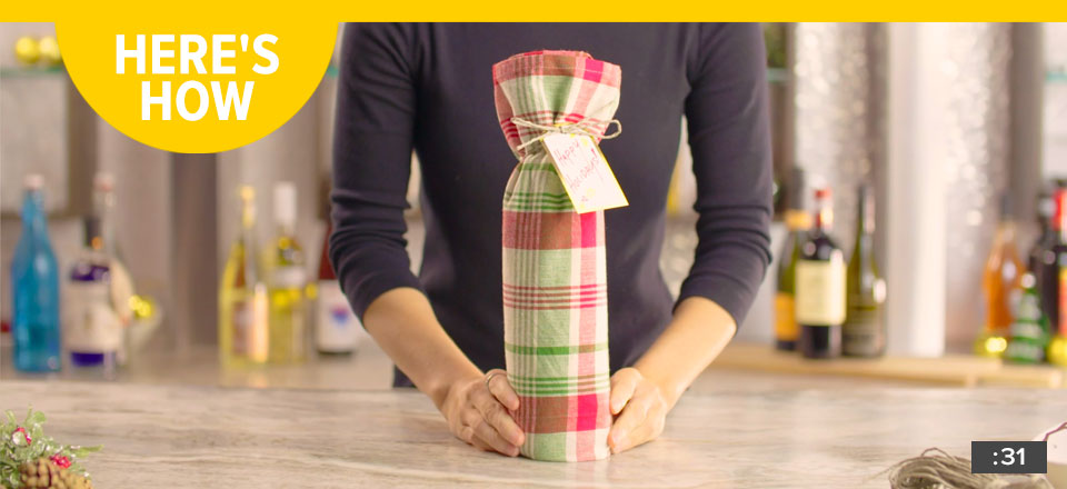 Here's How: Someone holding a bottle of wine in front of a bar that is wrapped in a nice fabric wrapping. Tied with twine and a handwritten note. A thirty-one second video