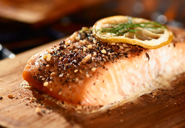 Seasoned cooked salmon with a thin slice of lemon, seated on a cedar plank