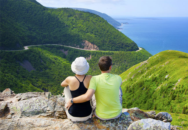 Couple sitting on a rocky precipice overlooking a coastline view with lots of greenery