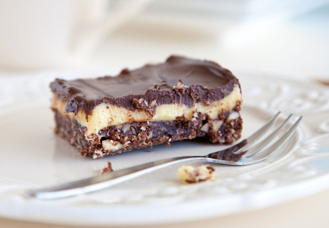Nanaimo bar on a white plate with a fork, a few bites taken out of the square