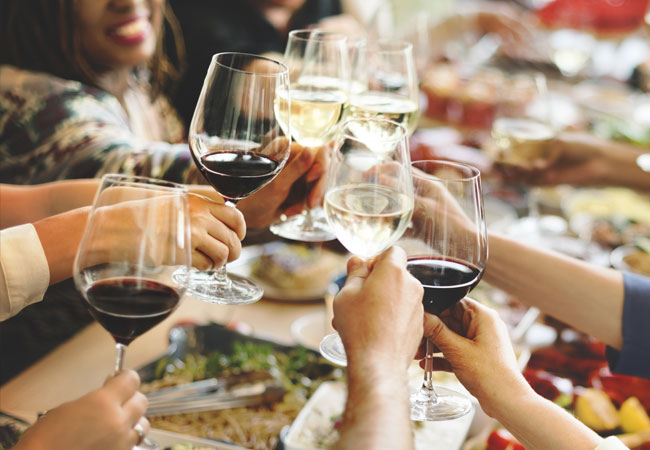 People toasting with glasses of red and white wine above a table with a full spread of food