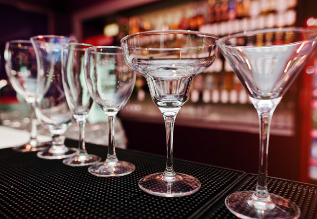 Different shaped cocktail glasses lined up on a bar