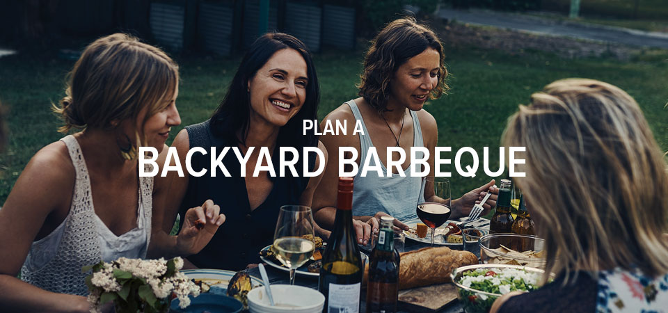 Four smiling women around an outdoor dinner table with food and wine with words that say 
