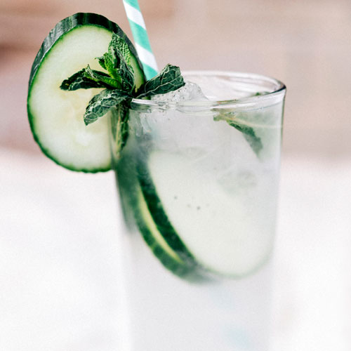 Close up of Mexican Rickey drink in a tall glass garnished with cucumber and a straw