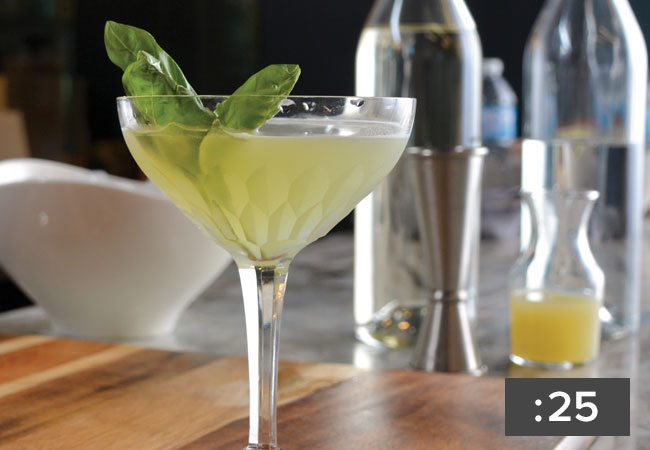 A drink in a fancy daiquiri glass garnished with basil