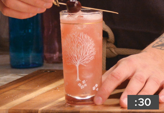 Buzzcut drink in tall glass garnished with cherry on a stick