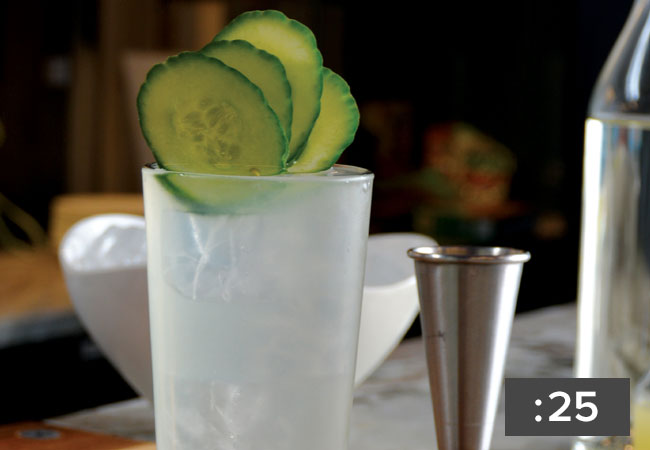 A close up of a cucumber gin drink garnished with four slices of cucumber
