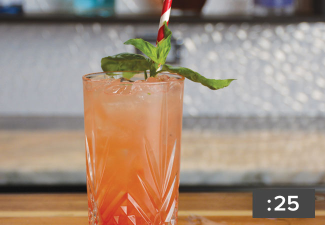 A close up of a summer blush drink garnished with basil