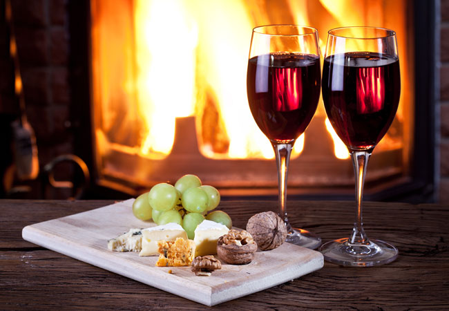 An appetizer board with two glasses of red in front of the fire