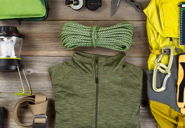 Flatlay image of camping gear -light jacket, backpack, lantern, rope, compass