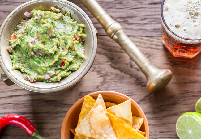 A bowl of guacamole with chips and a beer
