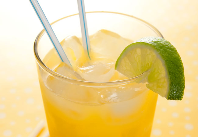 a yellow cocktail with two straws and a lime wedge