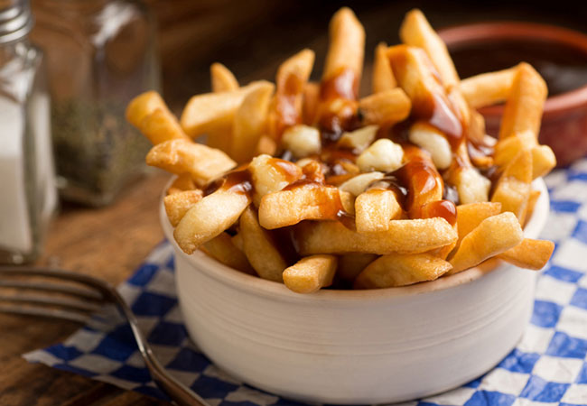 Poutine in a white bowl sitting on a blue and white check table cloth