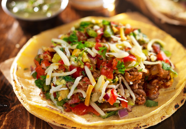 An open-shell taco topped with meat, veggies and cheese