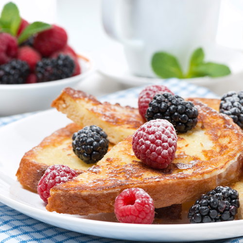 A stack of french toast halves accompanied by fresh raspberries and blackberries
