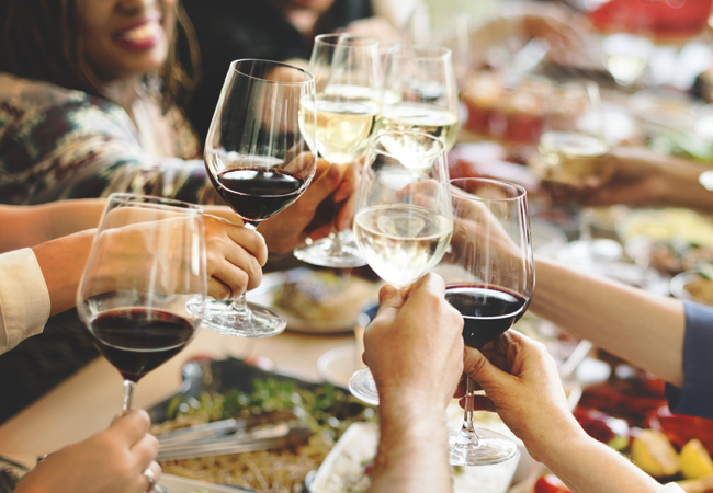 People toasting with glasses of red and white wine above a table with a full spread of food