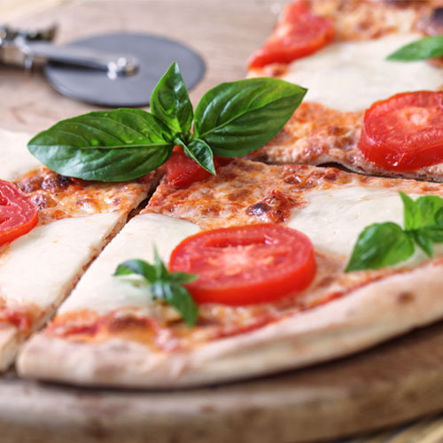 Margherita pizza with sliced tomato and basil on a wood cutting board