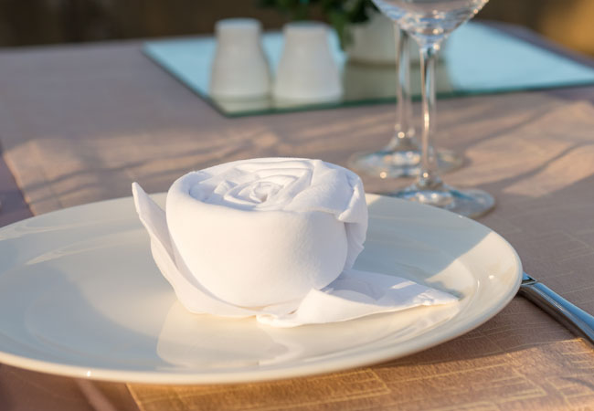 white napkin folded into a rose on a white plate