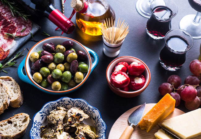 A table with olives, tomatoes, breads, wines and more dishes