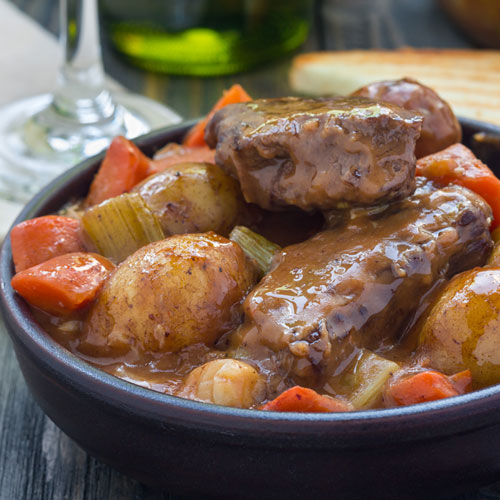 A bowl filled with beef, potatoes and carrots in a creamy sauce