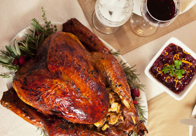 Flatlay image of a whole roasted turkey, a bowl of dressing and a glass of red wine. 