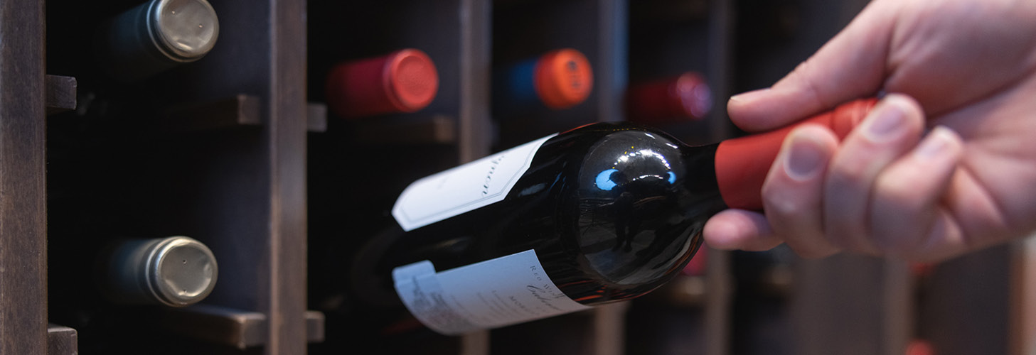 A person taking a bottle of wine from a wine rack