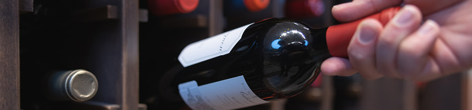 Picture of a hand taking a red wine bottle out of a wine rack.