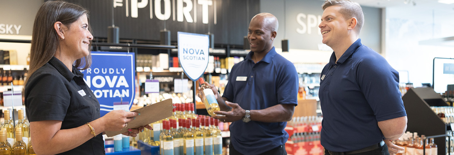 Three NSLC team members standing in a NSLC store. One is holding a clip board.