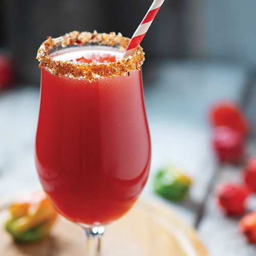 A closeup of a Clamato juice-based drink in a glass, the rim covered in child powder and salt with a paper straw.