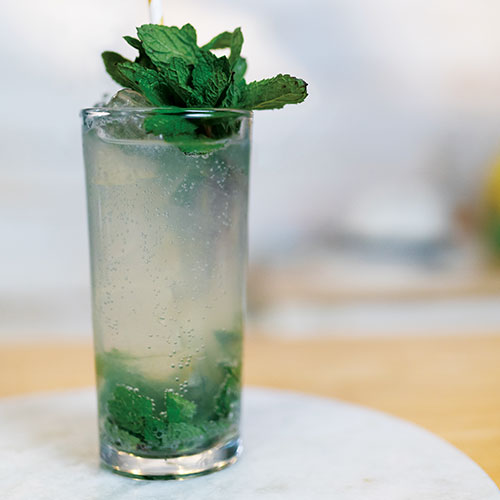 A closeup of a mixed drink in a highball glass, garnished with mint on top and crushed mint inside.