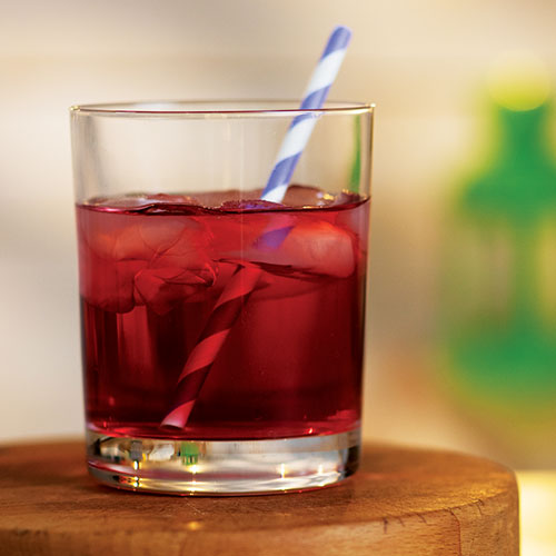 A closeup of a mixed red drink in an old fashioned glass with ice and a straw.