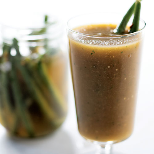 A closeup of a tomatillo-based drink in a footed highball glass garnished with Mexican spiced beans.