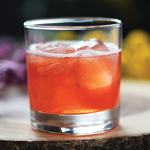 A closeup of a fizzy bright orange drink in an old fashioned glass with ice.