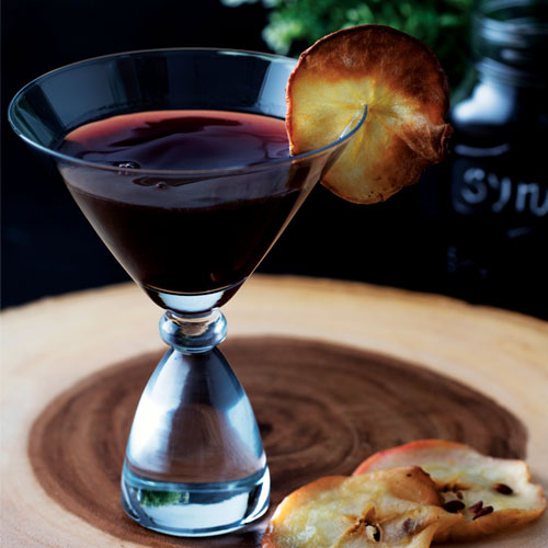 A martini in a fancy hourglass-shaped glass on a wooden platter with dried apple slices.
