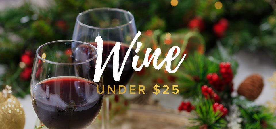 Two glasses of red wine on a gold platter on a table with Christmas decorations. Text that says “Wine Under $25”.